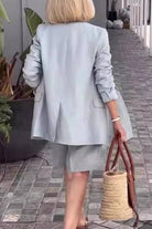 Woman wearing stylish blazer and shorts two-piece set walking on tiled path carrying woven bag