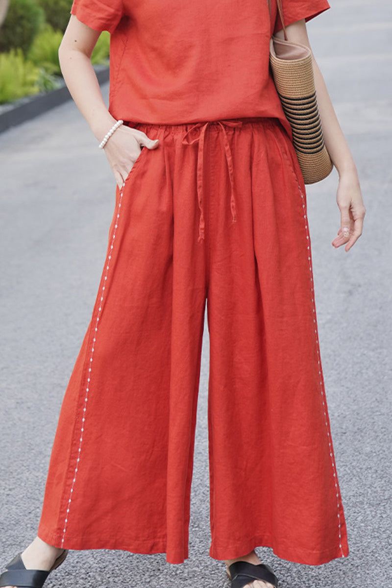 Women wearing wide-leg 100% linen pants in burnt orange with side stitch details and elastic waist, styled with matching top and casual sandals.
