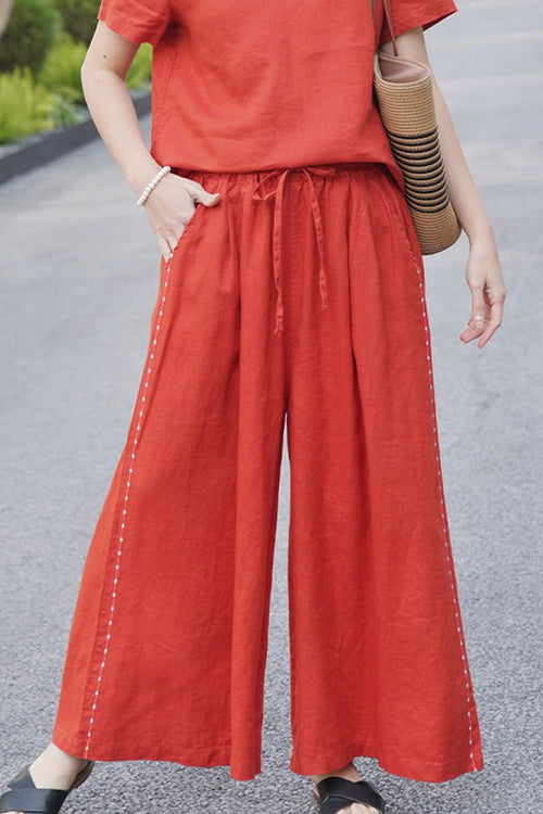 Women wearing wide-leg 100% linen pants in burnt orange with side stitch details and elastic waist, styled with matching top and casual sandals.