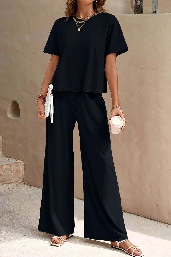 Woman wearing Riviera Relaxed Two Piece Set black wide-leg pants and loose short-sleeve top, casual elegant travel outfit