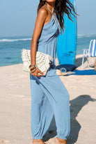 Woman wearing blue Sunshine On Sand halter-neck jumpsuit on a sunny beach with ocean background