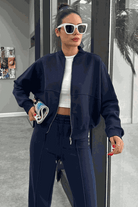 Woman wearing The Voyager Zip Set navy blue zip-front sweatshirt and wide-leg joggers, styled with white crop top and sunglasses