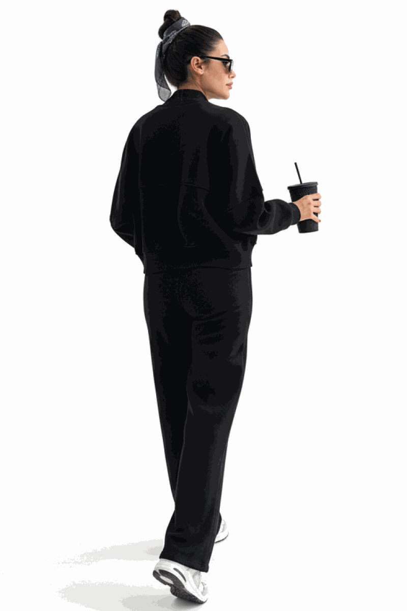 Woman wearing The Voyager Zip Set black zip-front sweatshirt and wide-leg joggers holding a cup