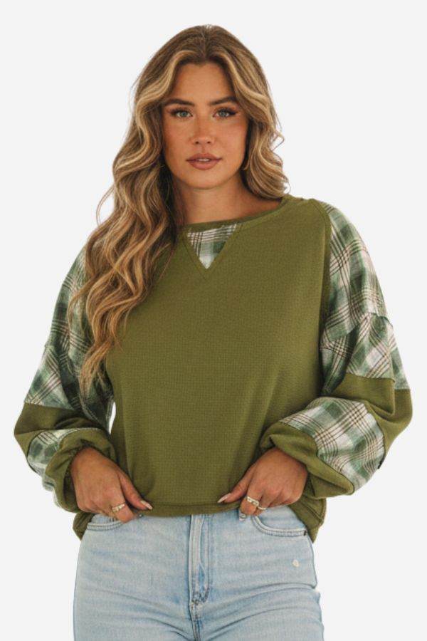 Green waffle knit sweatshirt with plaid sleeves and v-notch neckline worn by woman with wavy hair