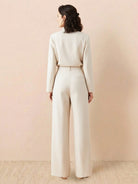 Woman wearing beige wide-leg thermal wool blend trousers with elastic back waist, standing against plain background, rear view.