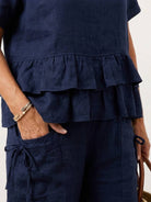 woman wearing navy blue cotton relaxed shorts and matching ruffle top two-piece co-ord set with side pockets and decorative tie detail