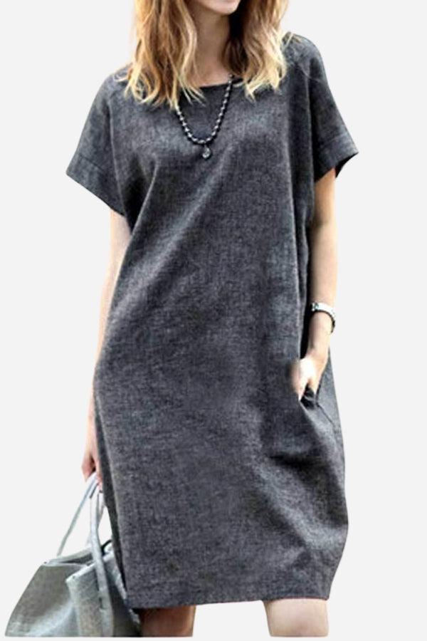 Woman wearing a charcoal gray short sleeve shift dress with side pockets, accessorized with a necklace and gray handbag