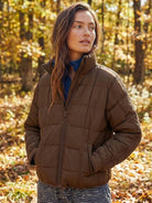 Woman wearing lightweight brown puffer travel jacket in autumn forest setting