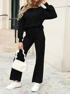 Woman wearing black round neck loose fit cozy two-piece set with long sleeves and wide-leg pants, holding white handbag and white sneakers, casual street style