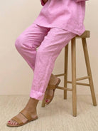 Pink asymmetrical two-piece trouser set with rolled-up sleeves and tapered pants paired with tan sandals sitting on wooden stool