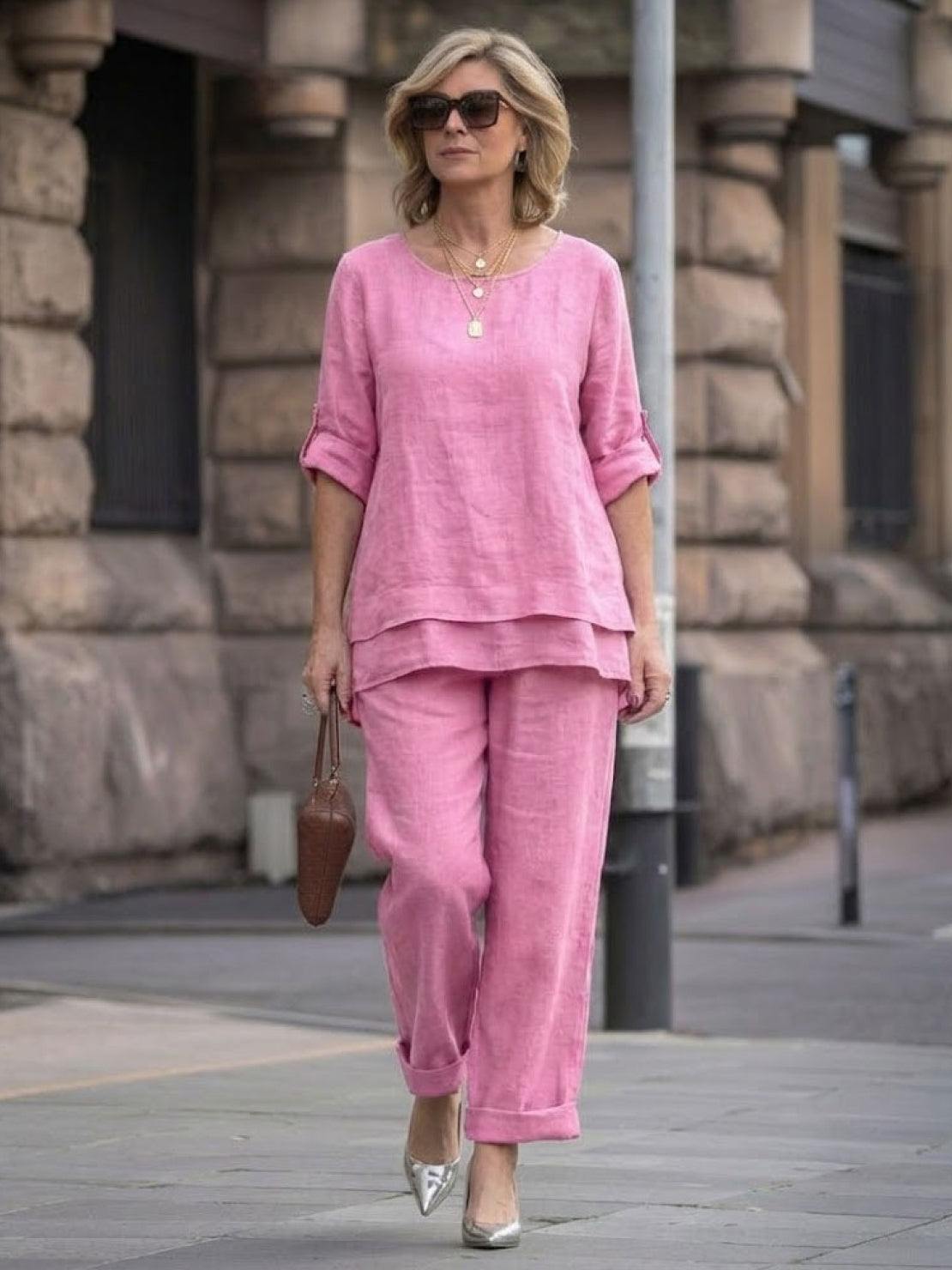 Woman wearing pink asymmetrical two-piece trouser set with rolled sleeves and loose fit walking outdoors