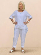 Older woman wearing white asymmetrical two-piece trouser set with rolled-up sleeves and tapered pants