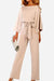 Woman wearing beige casual long sleeve belted jumpsuit with wide sleeves and round neck, holding a white clutch bag.