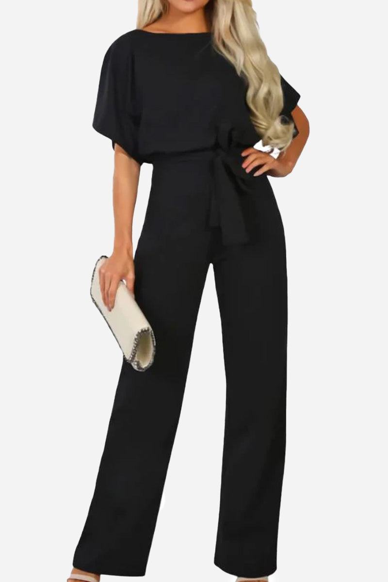 Woman wearing chic black short-sleeved wide-leg jumpsuit with belt and holding a white clutch purse