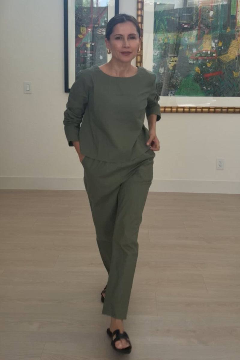 Woman wearing cotton-linen monochrome relaxed longline top and fluid wide-leg pants in muted green indoors