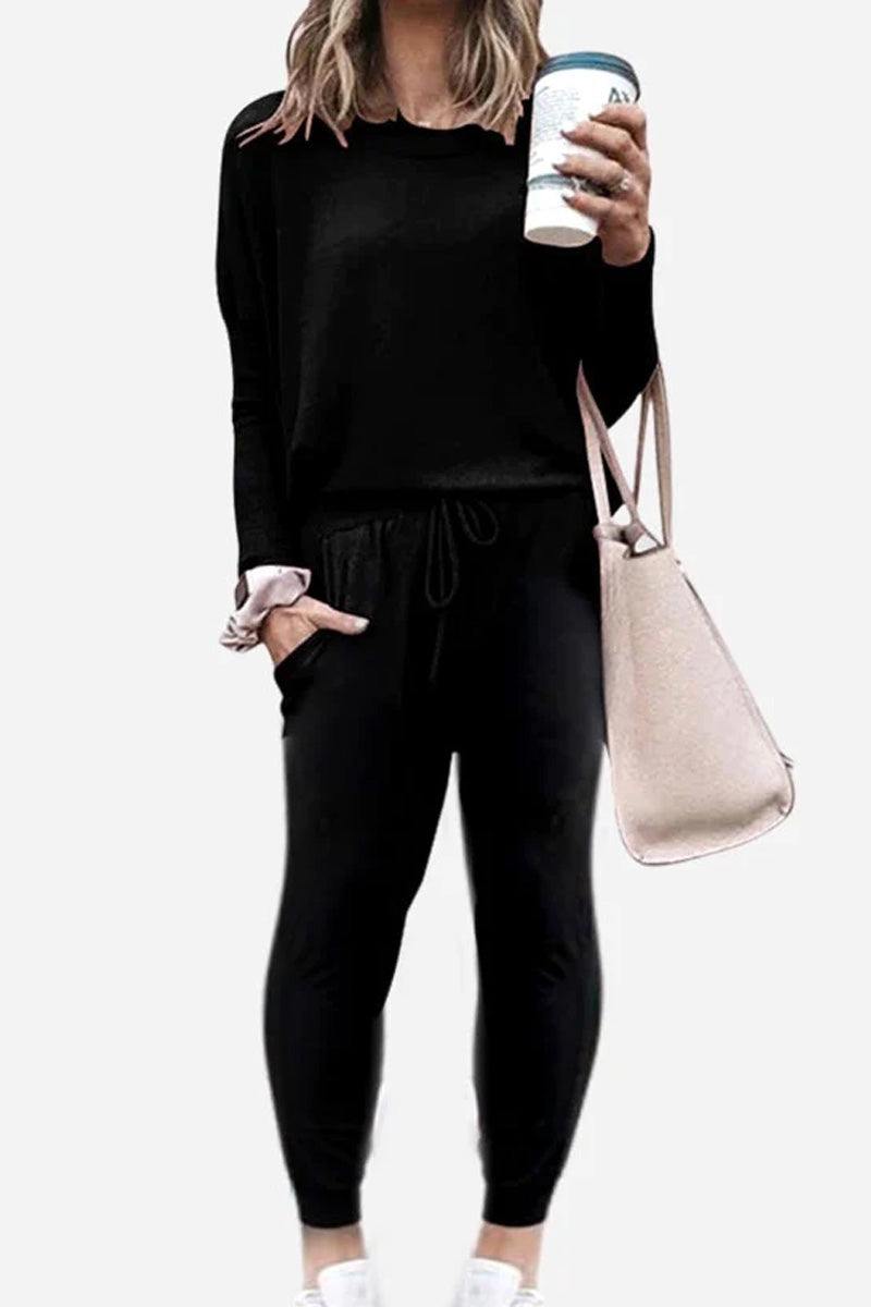 Woman wearing black Cozy Chic Two-Piece Sweatsuit with long sleeves and high-waisted pants holding a coffee cup and carrying a beige tote bag