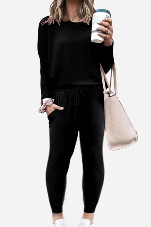 Woman wearing black Cozy Chic Two-Piece Sweatsuit with long sleeves and high-waisted pants holding a coffee cup and carrying a beige tote bag