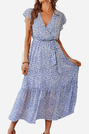 Woman wearing Elegant Blossoms Boho Maxi Dress with blue floral pattern, V-neck, short sleeves, and belted ruffle hem.