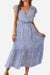 Woman wearing Elegant Blossoms Boho Maxi Dress with blue floral pattern, V-neck, short sleeves, and belted ruffle hem.