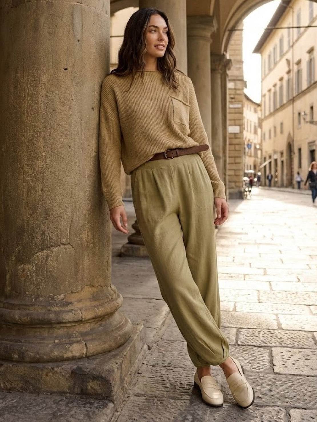 Woman wearing European minimalism style relaxed sweater top and trousers in neutral tones walking in historic city street