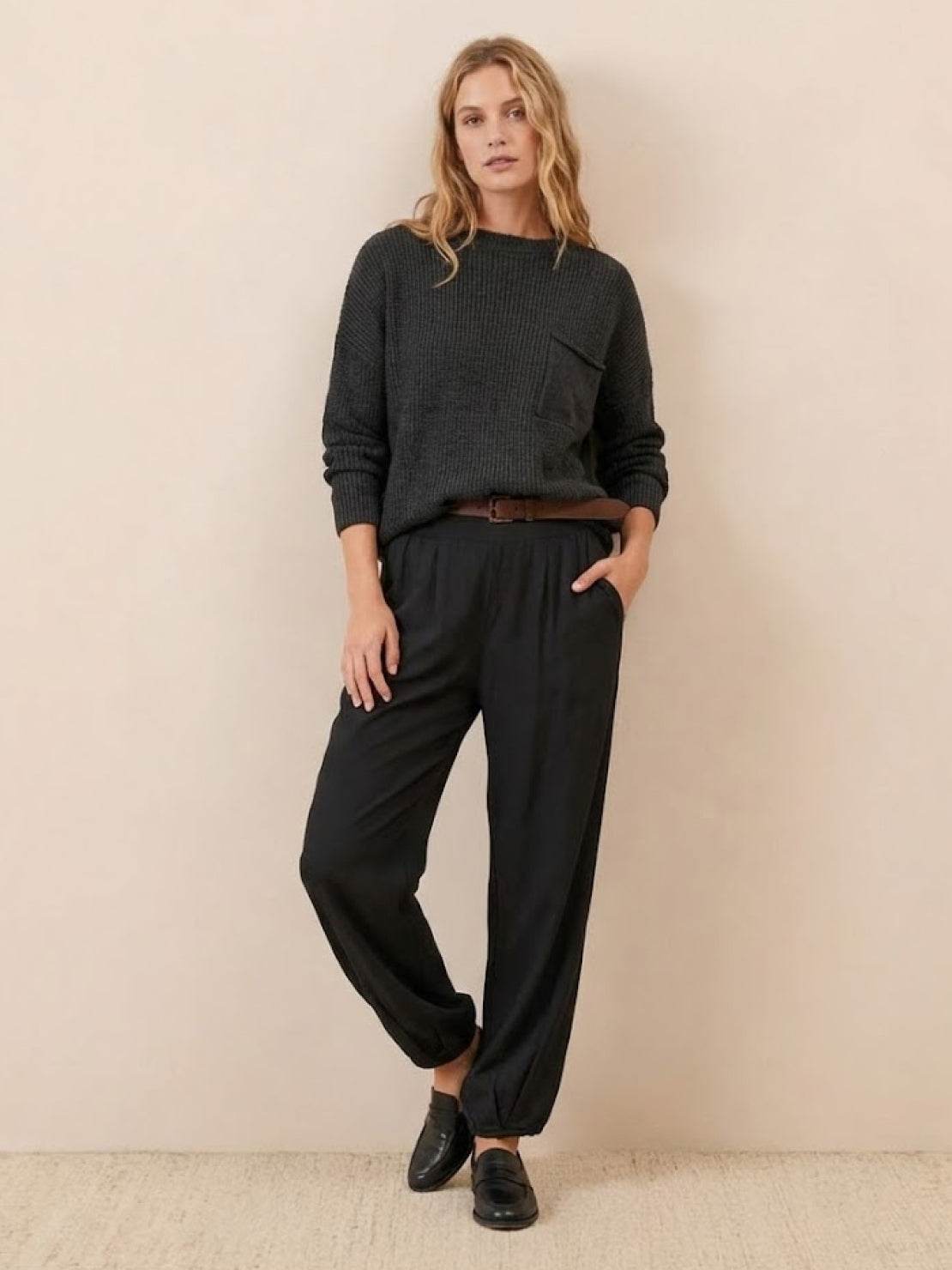 woman wearing European minimalism relaxed black sweater top and trouser set with knit pocket and belt