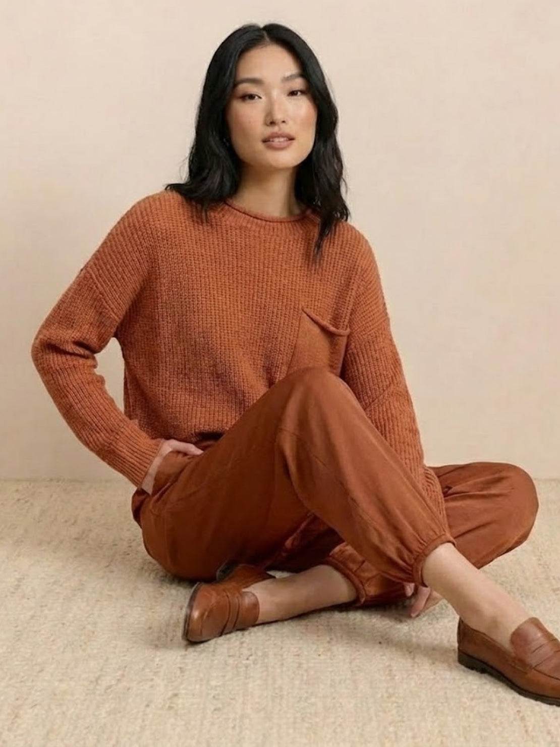 Woman wearing European minimalism relaxed sweater and trouser set in rust color sitting on floor
