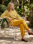 Woman wearing mustard yellow relaxed knit sweater and trousers sitting outdoors in European minimalist style outfit