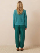 Back view of a woman wearing a teal knit sweater and matching relaxed trousers in European Minimalism style
