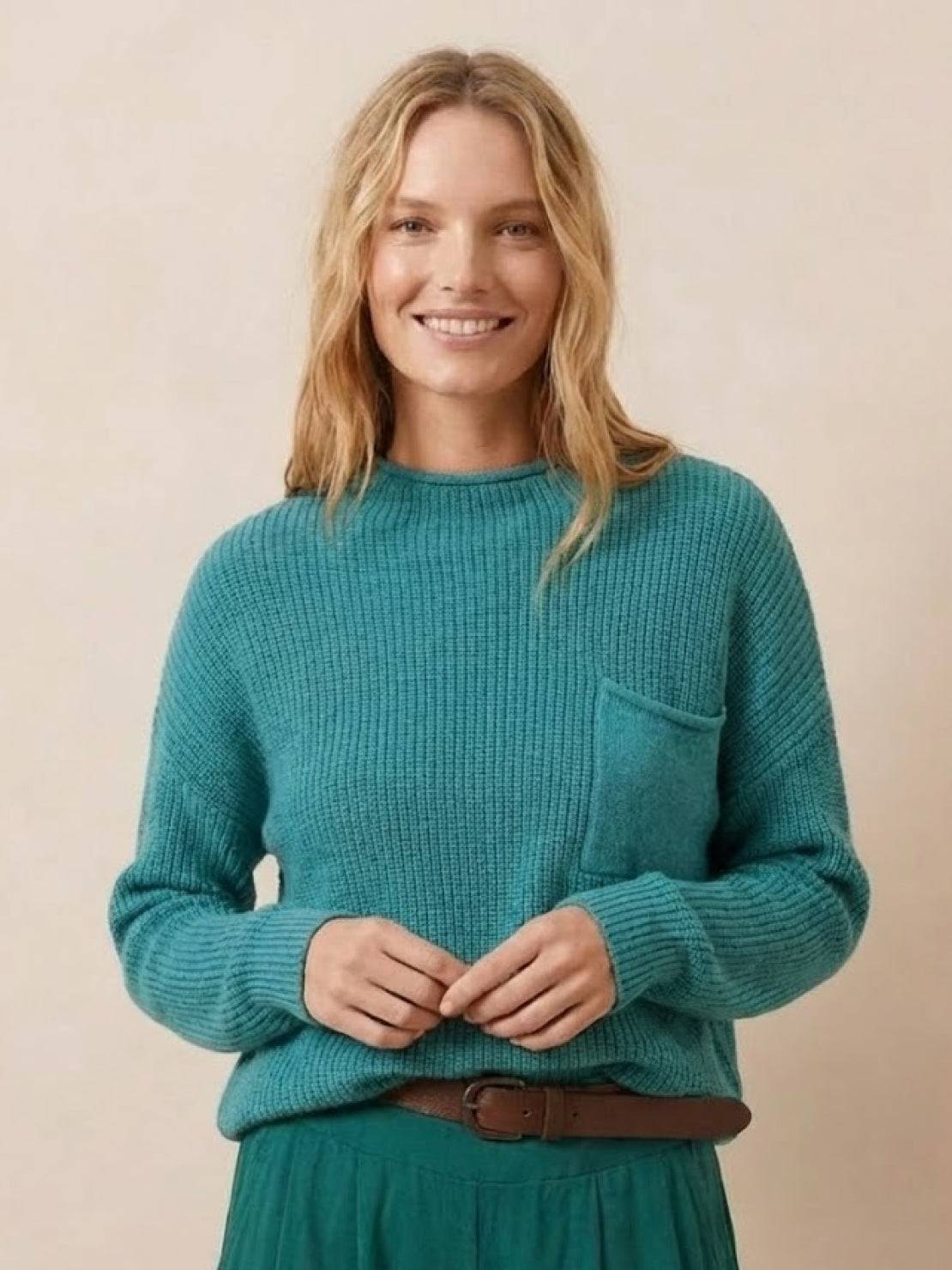 Woman wearing a teal knit sweater with pocket detail, embodying European minimalism style.