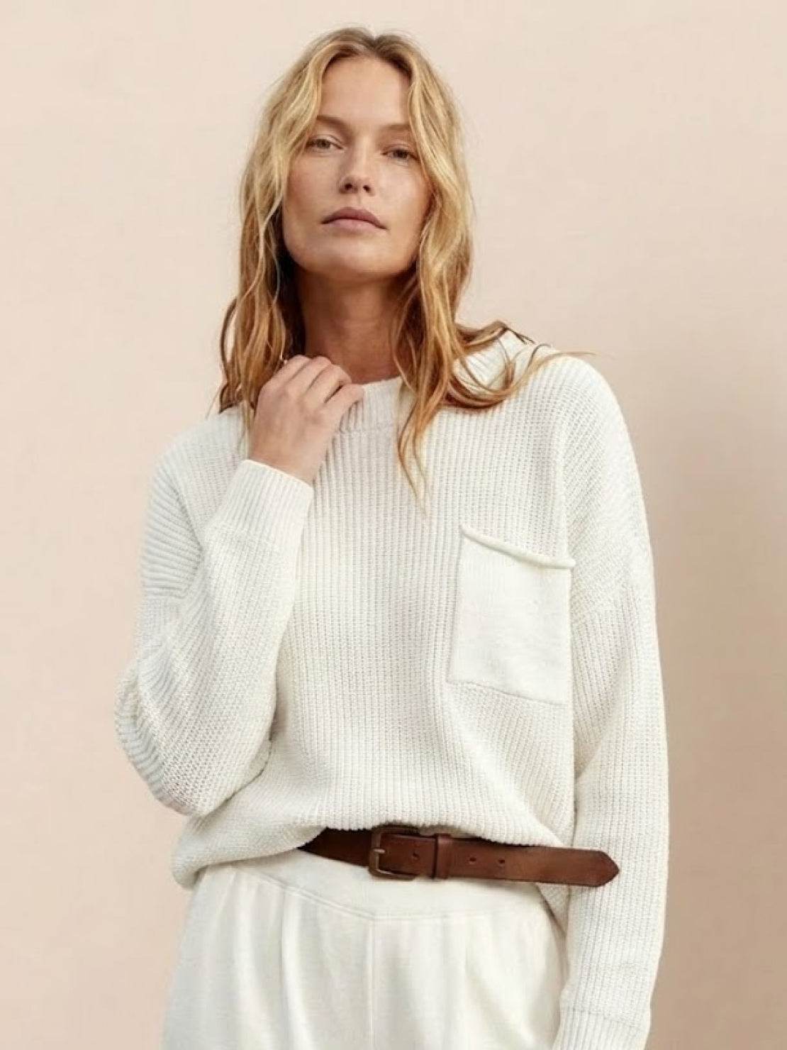 woman wearing European minimalism relaxed white knit sweater top with pocket and white trousers styled with brown belt