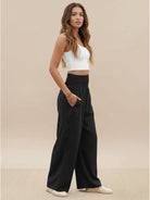 Woman wearing black high-waist cotton linen palazzo pants with wide legs and pockets, styled with a white crop top and casual shoes.