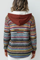 Back view of a woman wearing a striped multicolored Highland Plaid Shacket with a rust-colored hood and fleece lining.