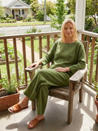 Woman wearing loose solid color green two-piece set sitting on wooden chair outdoors