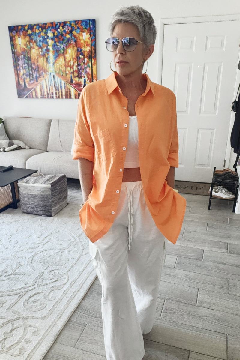 Woman wearing oversized linen shirt in soft orange with white pants in modern living room