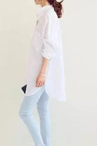Woman wearing a white oversized linen shirt with rolled sleeves and light blue jeans, side view