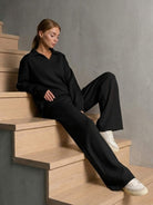 woman wearing black plush and preppy two-piece set with wide-leg pants and polo collar top sitting on wooden stairs