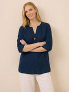 Woman wearing navy blue pure linen age-defying button detail shirt with three-quarter sleeves and white pants