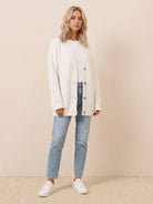 woman wearing relaxed fit oversized white button down knitwear cardigan with jeans and white sneakers indoors