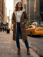 woman wearing brown sherpa-lined hooded teddy coat with jeans and boots on city street with yellow taxi