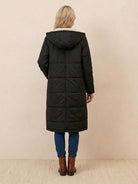 Back view of a black Sherpa-lined hooded teddy coat with an extra-long puffer design worn by a woman with blonde hair, paired with blue jeans and brown boots.