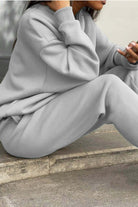 Woman wearing a soft grey cotton blend tracksuit with relaxed fit and cuffed sleeves and pants sitting outdoors