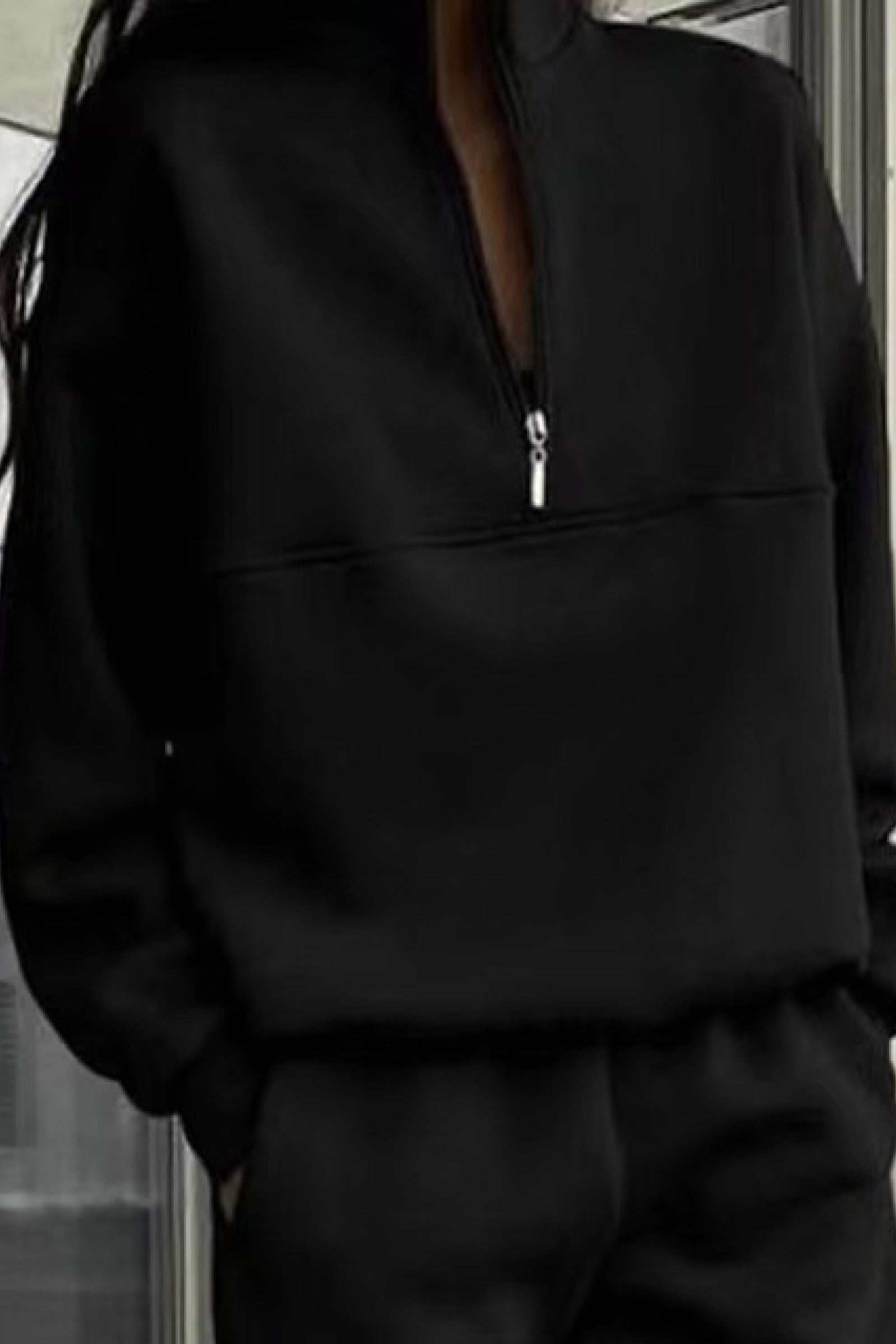 Woman wearing a black cotton blend tracksuit with a half-zip high collar and relaxed fit