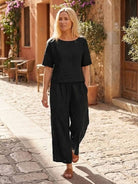 woman wearing black loose fit co-ord set with short sleeves and wide-leg trousers walking outdoors on sunny stone pathway