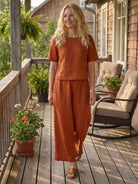 Woman wearing rust-colored loose fit co-ord set with short sleeves and wide-leg pants on wooden porch