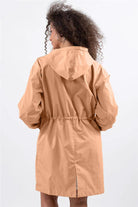 Back view of woman wearing oversized tan Rain Couture Windbreaker with adjustable hood and cinched waist