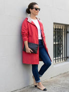 Woman wearing a red oversized Rain Couture Windbreaker with jeans and flats, standing against a wall outdoors