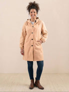 Woman wearing beige Rain Couture Windbreaker oversized water-resistant jacket with hood and pockets, paired with jeans and brown boots
