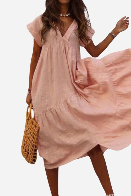 Woman wearing a pink V neck tiered cotton midi dress with short sleeves and frill hem holding a woven handbag