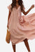 Woman wearing a pink V neck tiered cotton midi dress with short sleeves and frill hem holding a woven handbag