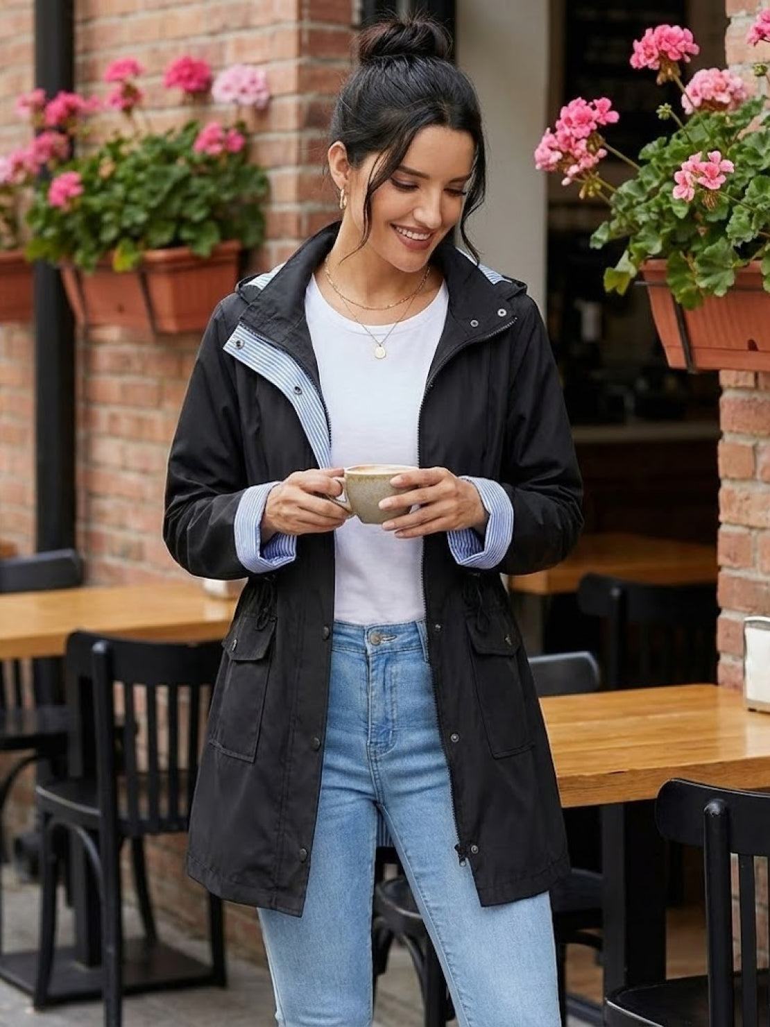 Women wearing black water resistant hooded windbreaker jacket with striped inner lining and pockets outdoors